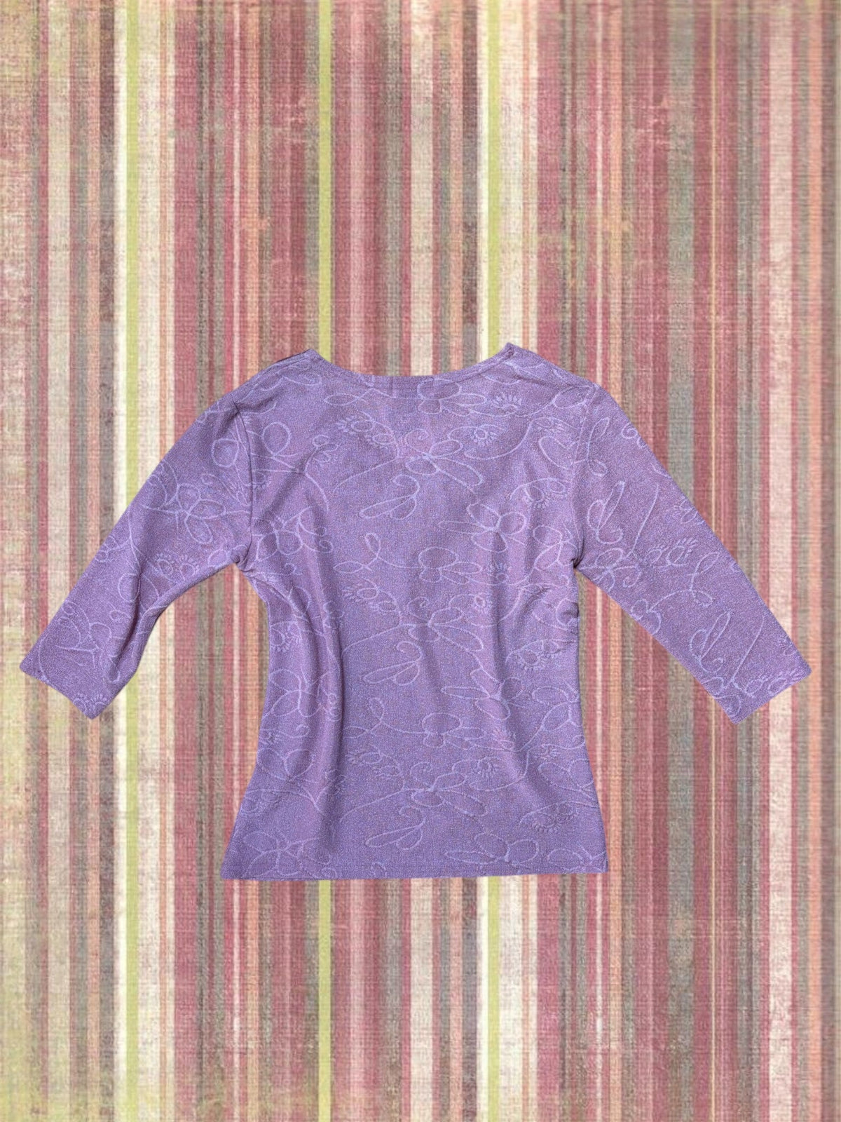 A lavender purple long-sleeve top with a subtle tonal floral jacquard pattern, laid flat against a vertically striped multicolor background.